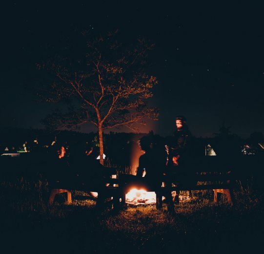 Four gravel bikers sit relaxed around a campfire at night.