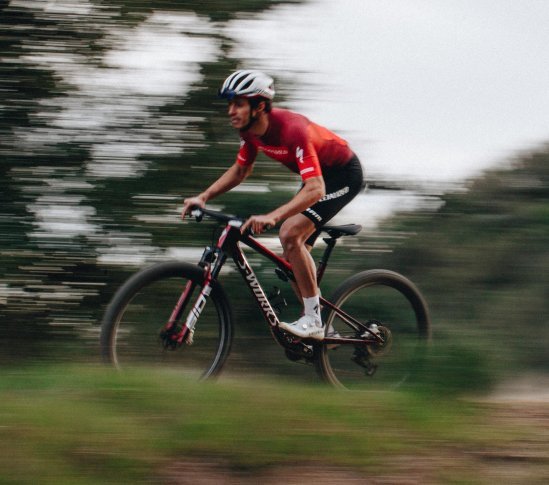 Ciclista en una Specialized Epic 9 de montaña pedaleando rápido por un sendero forestal con desenfoque de movimiento
