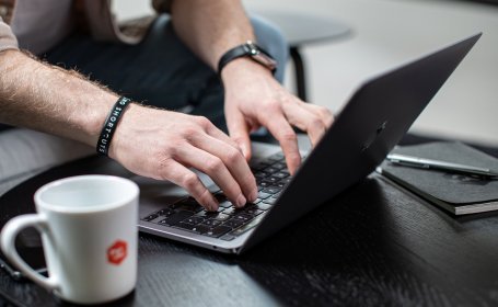 Hände tippen auf einem Laptop neben Kaffeetasse, Detailaufnahme des Schreibprozesses für den bike-components Blog