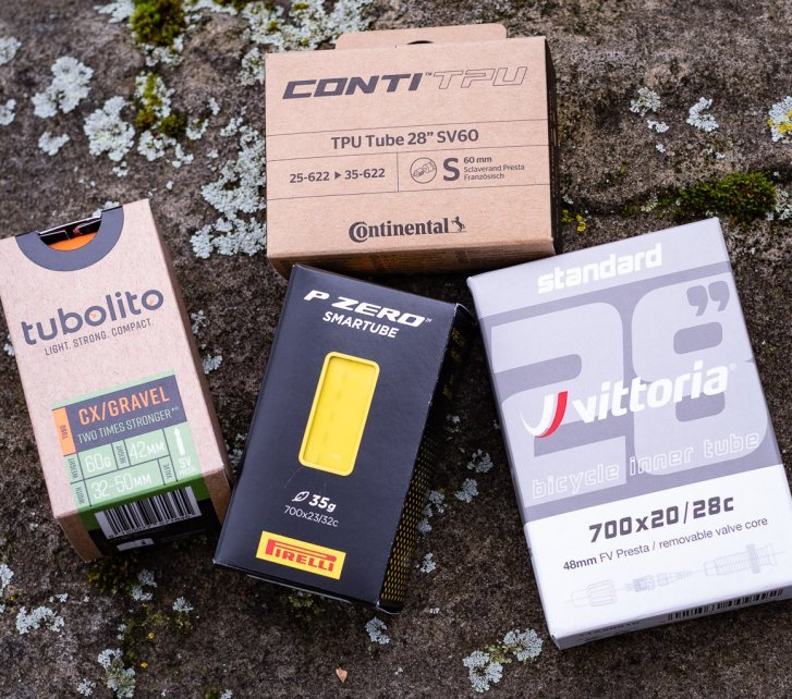 Vier Fahrradschläuche in ihren Kartons liegen auf einem Stein: Conti TPU, Tubolito Gravelm Pirelli P-Zero Smartube, Vittoria Standard 