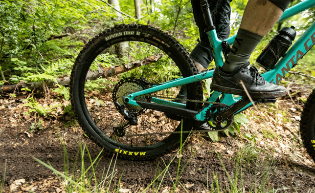 A mountain biker rides a Santa Cruz through the forest. The focus of the photo is on the bike’s rear triangle. 