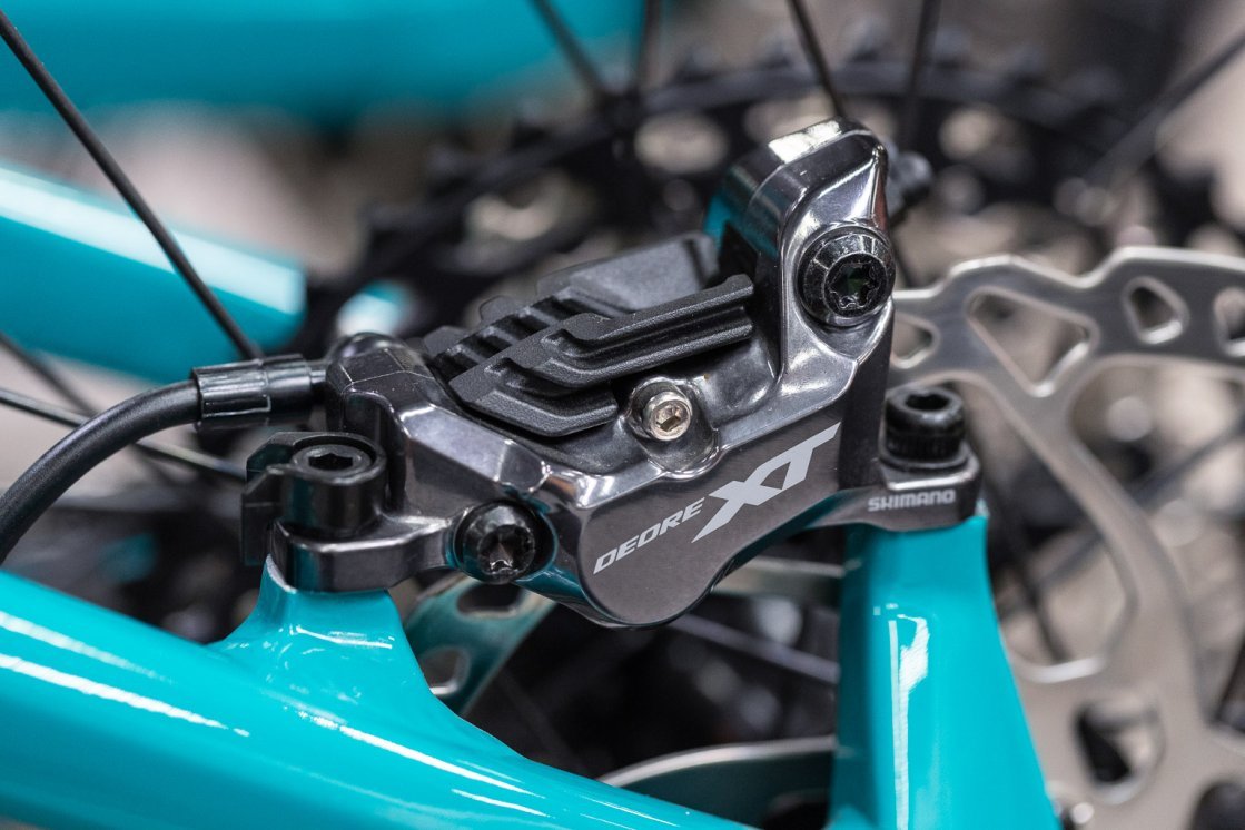 Gros plan sur un étrier de frein à disque Shimano Deore XT monté sur un cadre de vélo turquoise.