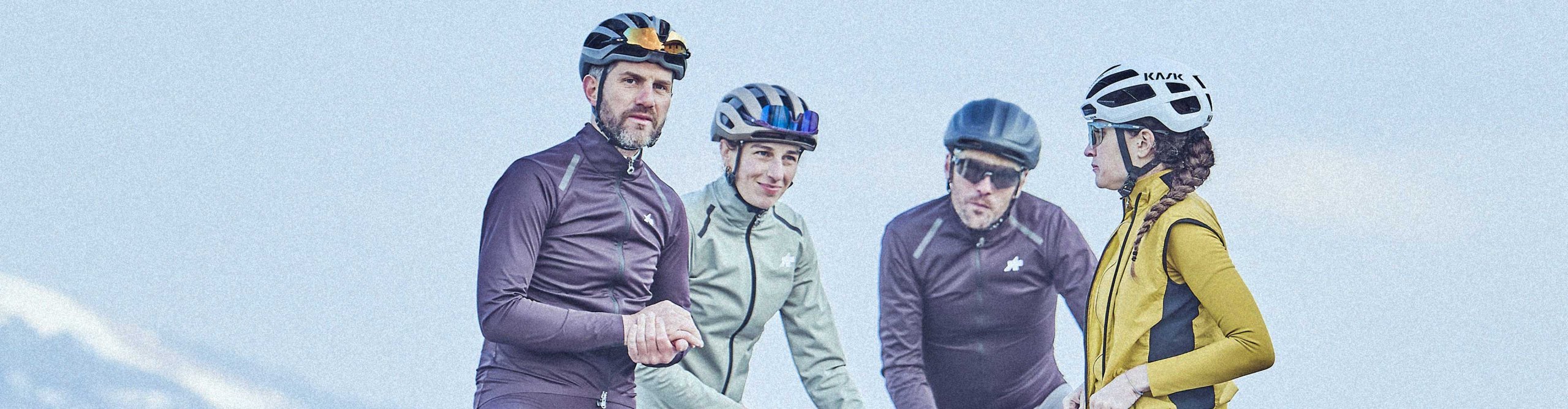 Quatre cyclistes sur route en tenue de vélo posent avec leurs vélos devant un vaste paysage montagneux.