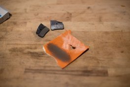 Ein Stück orangefarbenes Schleifpapier mit sichtbarem Abrieb von Bremsbelägen liegt auf einer Holzoberfläche, nachdem es verwendet wurde, um die Beläge anzurauen.