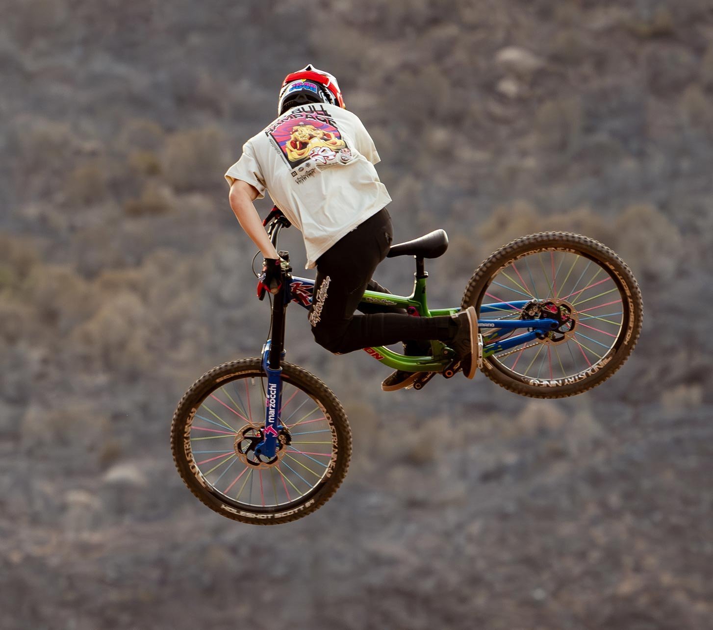 Troy Lee Designs mountain biker performing a freestyle jump on a freeride MTB in a rocky desert landscape