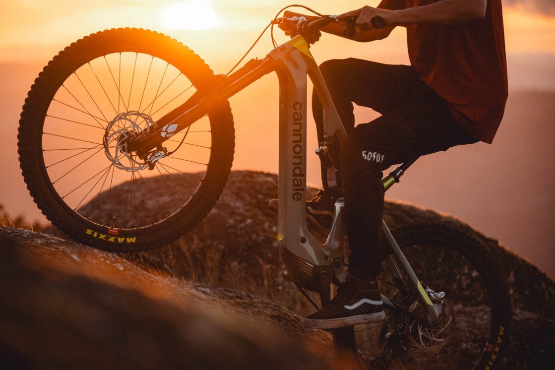 A man on an E-MTB rides up a rock in the orange backlight of the setting sun