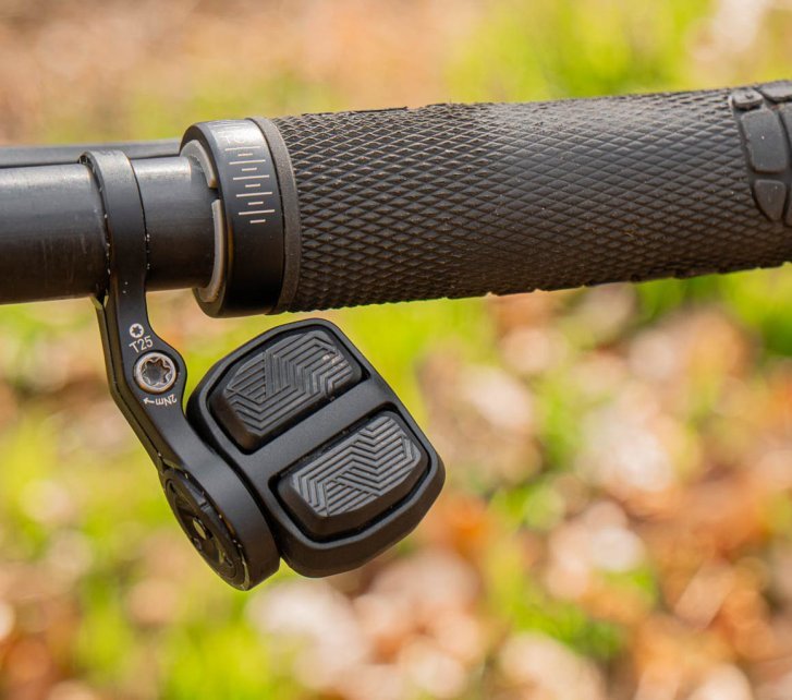 Foto de detalle de un controlador SRAM AXS Pod en el extremo derecho del manillar de una MTB. La empuñadura negra parece usada, al fondo se ve naturaleza verde desenfocada.