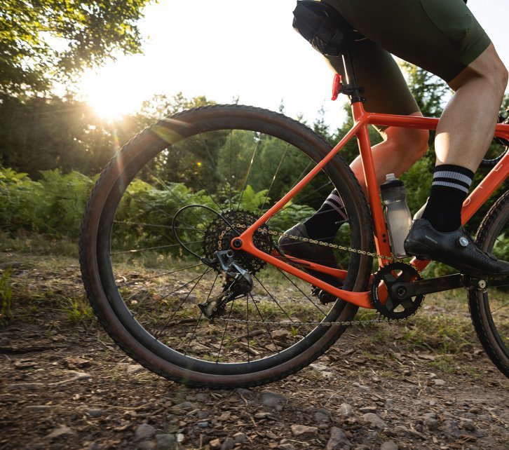 Björn from the bc Team rides an OPEN gravel bike over a dirt road. The bike is the focus of the picture.