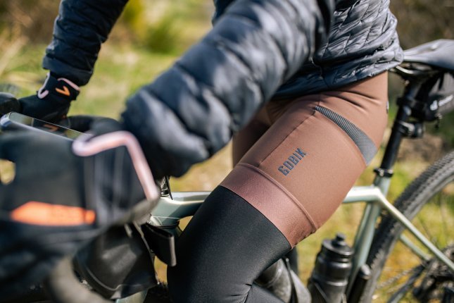 Detailfoto: Wir sehen das linke Bein einer Frau auf einem Gravelbike. Eine braune Bike-Shorts mit Gobik Logo ist im Fokus.