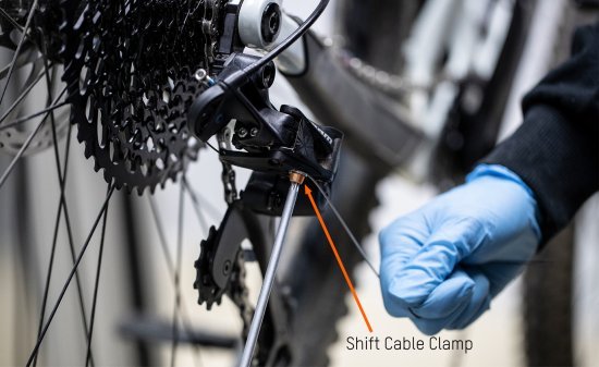 While the bc mechanic tightens the clamp bolt with a hex key, he pulls the shift cable with his other hand.