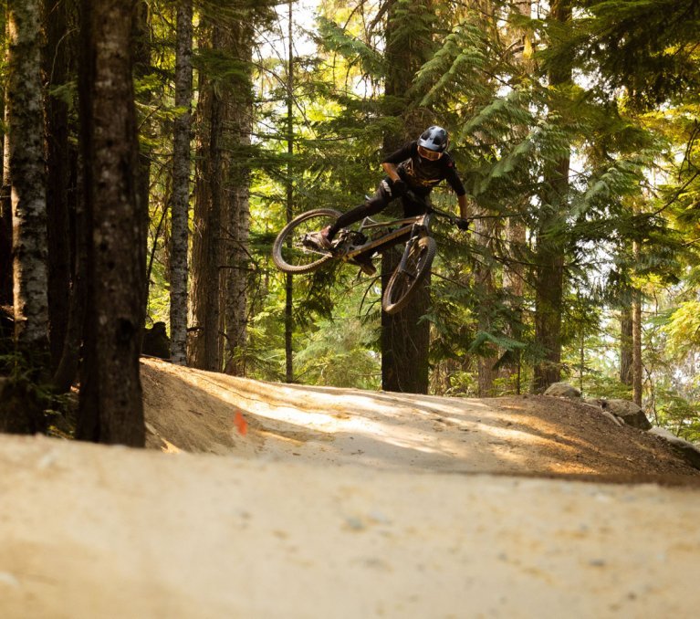 Christoph aus dem bc Team stellt während eines Sprungs mit seinem MTB das Rad quer. Er befindet sich im Wald.