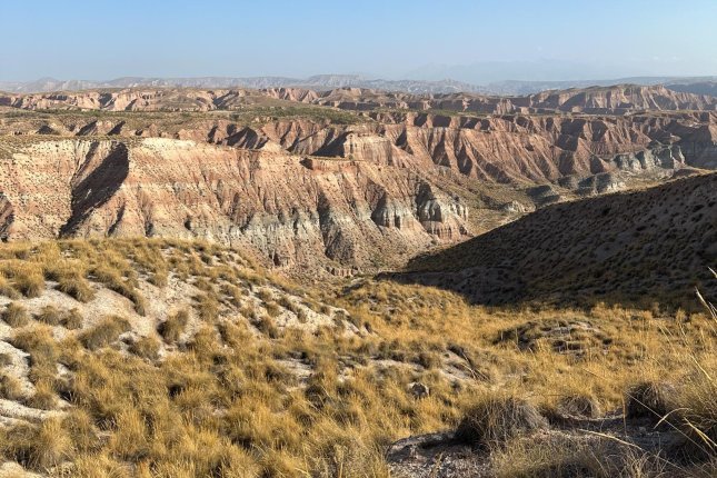 Totale einer Erosionslandschaft in der Spanischen Wüste. Man erkennt eine Bänderung der Steilhänge durch die Schichtung verschiedenfarbiger Gesteine. Der Himmel ist wolkenlos blau