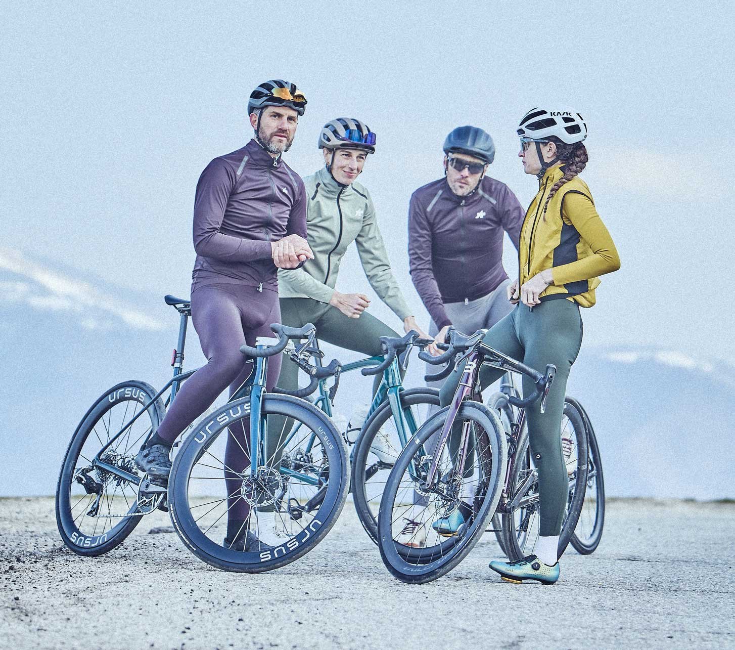 Quatre cyclistes sur route en tenue de vélo posent avec leurs vélos devant un vaste paysage montagneux.