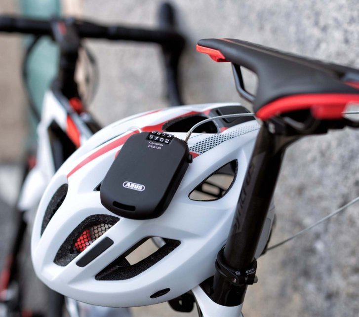 Candado de cable compacto con combinación pasado por las aberturas de un casco de bicicleta y sujeto a la bici.