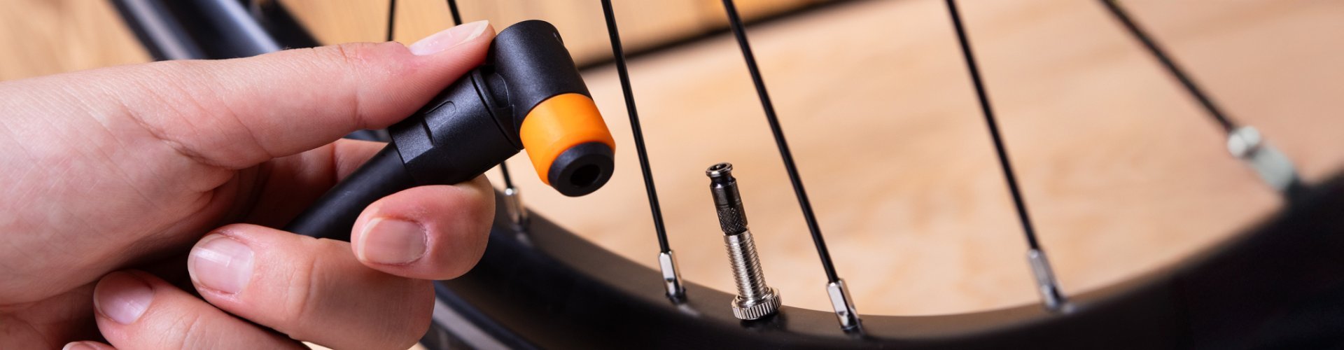 A woman’s hand holds a black and orange pump head next to a Schwalbe Clik Valve bicycle valve on a bike wheel.