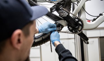 A chain whip and cassette removal tool are attached to the cassette. The cassette is loosened by the mechanic.