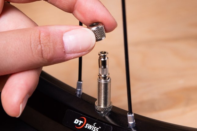 Close-up: A hand holds the locknut of a Dunlop valve, next to a silver Clik Valve insert already placed in the mounted valve stem.