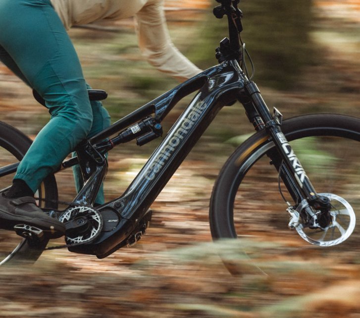 A woman on an E-MTB speeds through the forest. Close-up side view of the bike, rider partially cut off