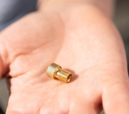 A brass-coloured car valve adapter lies on a palm
