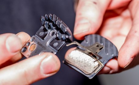 Gros plan de deux mains préparant de nouvelles plaquettes de frein Shimano avec leur ressort avant de les installer dans l’étrier.