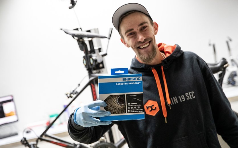 Thomas, mécanicien chez bc, tient une nouvelle cassette Shimano à 11 vitesses devant l’appareil photo. 