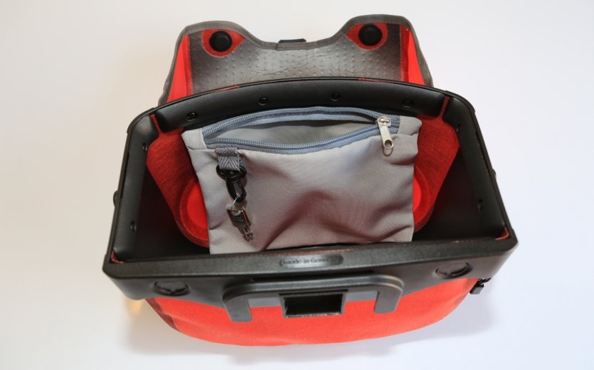 The interior of a red Ortlieb bicycle bag with multiple compartments, including a small gray zippered pocket with a keychain attached to it.