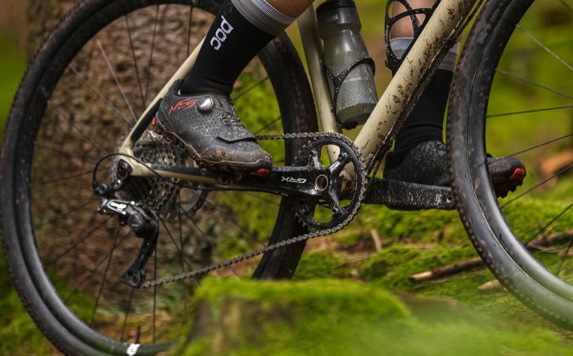 Cyclist riding a gravel bike with GRX shifters across a trail.