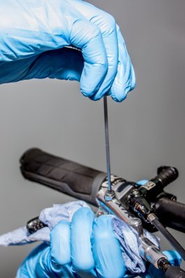 A hand in blue gloves tightens a bleed screw on the brake lever of a bicycle to complete the bleeding process of a hydraulic disc brake.