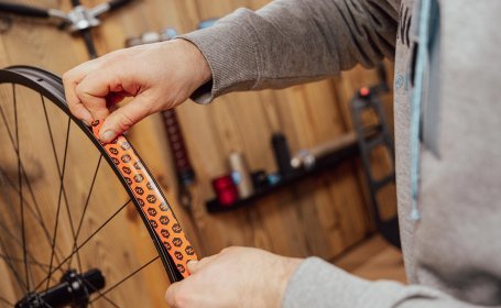 Hand bringt Tubeless-Felgenband in eine Fahrradfelge ein und beginnt einige Zentimeter vor der Ventilöffnung.