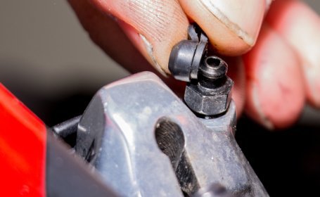 Gros plan d’un doigt retirant le capuchon en caoutchouc d’une vis de purge sur un étrier de frein hydraulique de vélo.