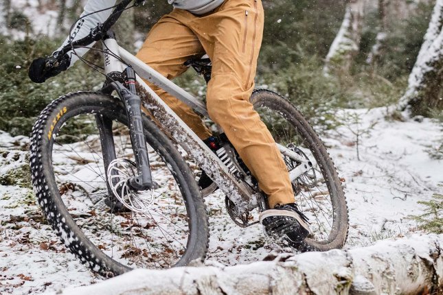 Ciclista de montaña pasando sobre una raíz en un sendero forestal con nieve.
