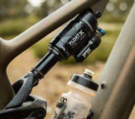 Detailfoto des Hinterbaudämpfers an einem Turbo Levo 4: Am unteren Bildrand ist eine Trinkflasche zu sehen. Das E-MTB scheint im Wald zu stehen. 