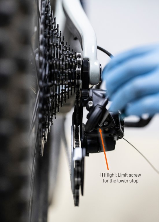 Using a hex key, bc mechanic Thomas sets the inner stop of the rear derailleur. An orange arrow marks the exact spot.