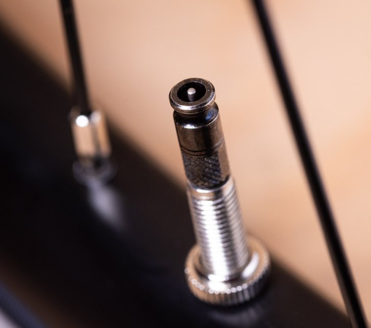 Close-up: A Schwalbe Clik Valve mounted on a bicycle, seen from above. The small pin in the center of the metallic black valve head is visible.