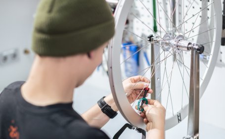 Ein Laufrad ist in einen Zentrierständer eingespannt. Ein Mechaniker prüft die Speichenspannung. 