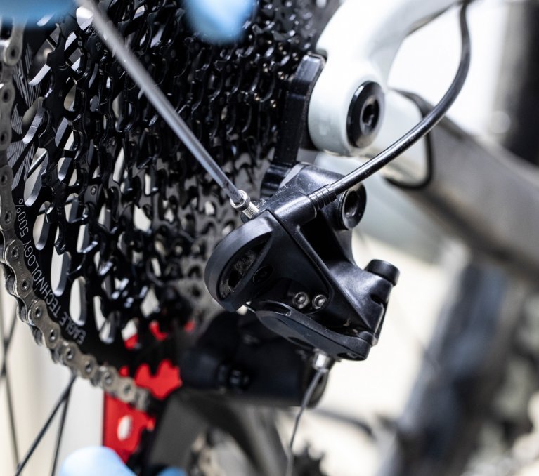 The bc mechanic turns the B-bolt of the MTB rear derailleur with a hex key.