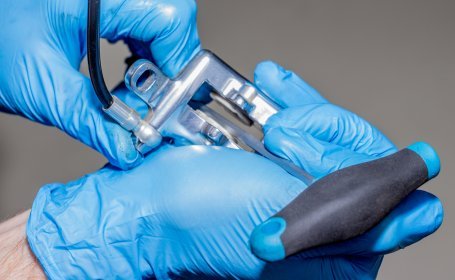 Gros plan d’une personne portant des gants bleus utilisant un outil pour écarter un étrier de frein de vélo afin de nettoyer ou repousser les pistons.