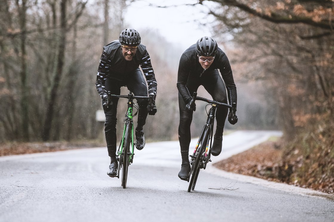 Two men on road bikes are racing towards the camera with big grins.