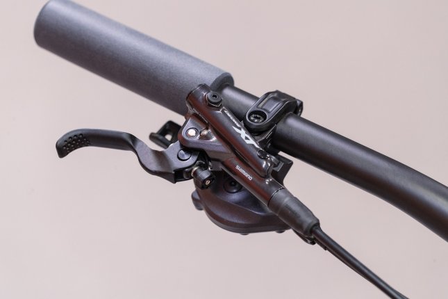 Vista superior del extremo derecho de un manillar de bicicleta con puño de goma y una bomba de freno Shimano XT con cilindro maestro.