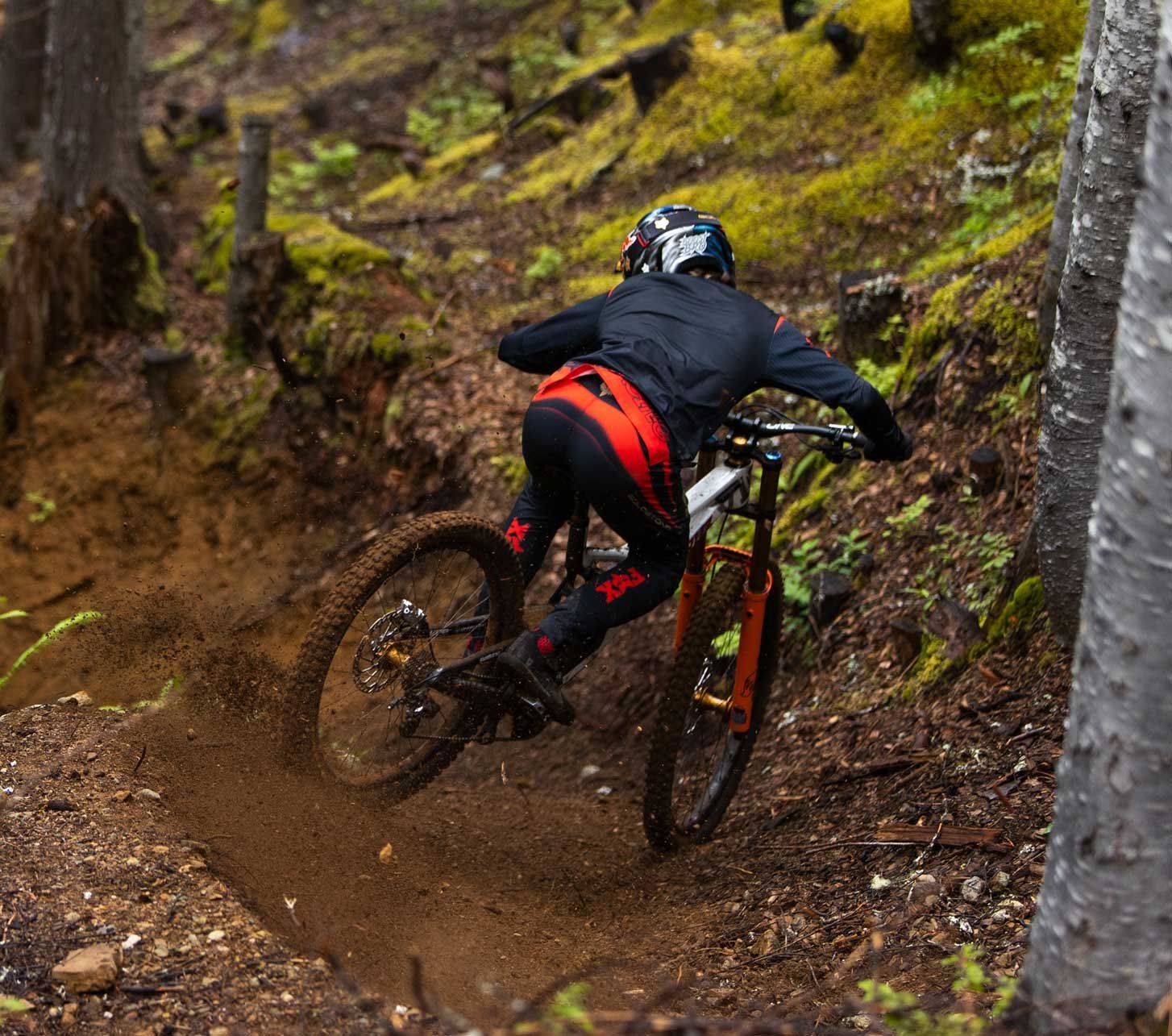 Vététiste en tenue Fox Racing négociant un virage prononcé sur un sentier forestier avec une fourche Fox.