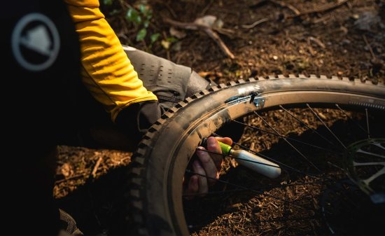 Ciclista de montaña reparando un pinchazo en el sendero e inflando la rueda.