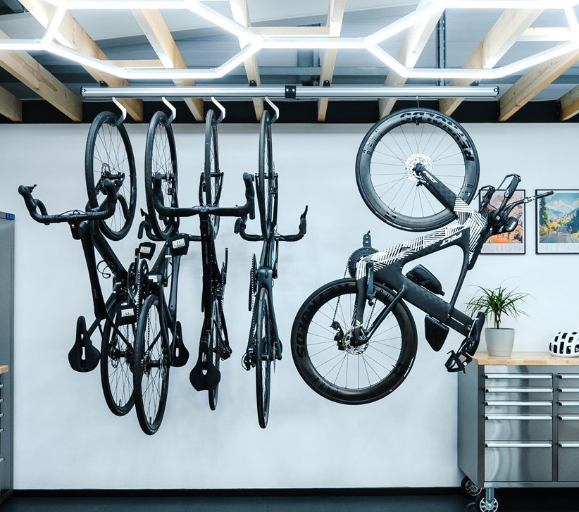 Bike garage with four hanging road bikes and a triathlon bike on a wall rack, with workbench and helmet beside it.