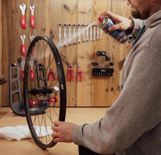 Personne nettoyant une jante de vélo dans un atelier avec un spray nettoyant frein, préparation avant la pose du fond de jante.
