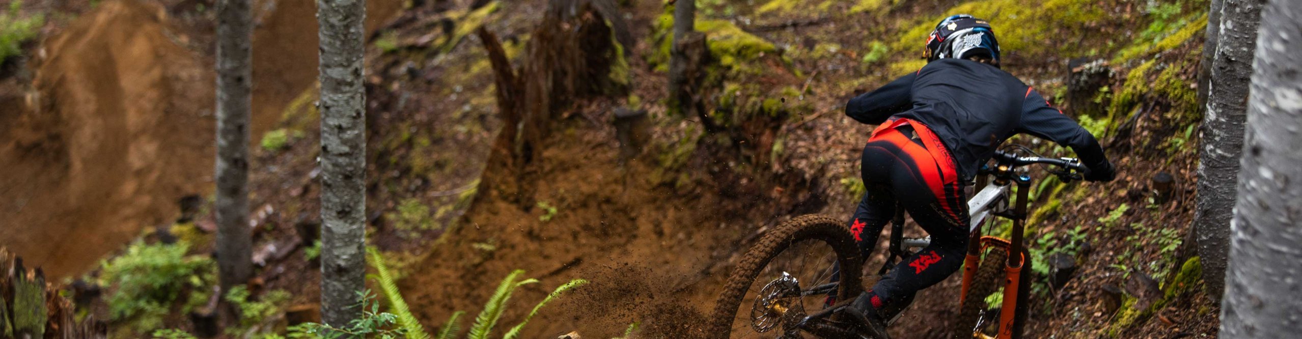 Vététiste en tenue Fox Racing négociant un virage prononcé sur un sentier forestier avec une fourche Fox.