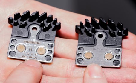 Gros plan d’une main tenant deux plaquettes de frein Shimano J04C METAL neuves pour les côtés droit et gauche.