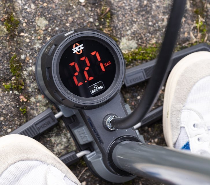 Detailfoto, das digitale Manometer einer SKS Standpumpe. Zwei Füße in weißen Sneakern stehen auf den Fußrasten der Pumpe 