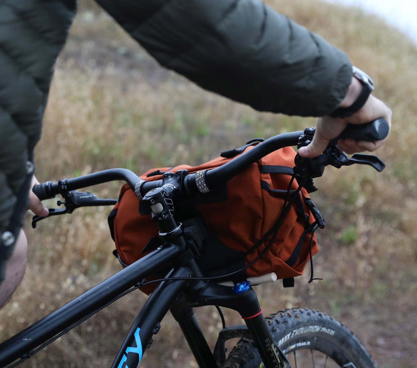Fahrer greift an den Ritchey Lenker eines Mountainbikes mit Lenkertasche auf einem schmalen Trail.