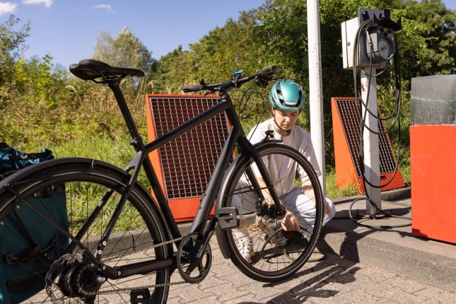 A young woman crouches behind the front wheel of her commuter bike, inflating it with a petrol station compressor