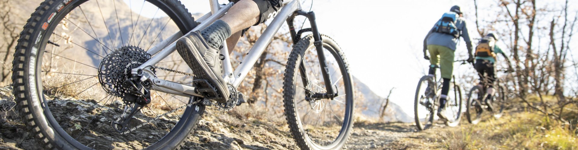 A group of mountain bikers ride up a rocky climb in sunny weather.