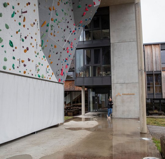 bc-Brandmanagerin Svenja steht an eine Wand gelehnt unter einer Kletterwand am Vaude-Firmensitz.